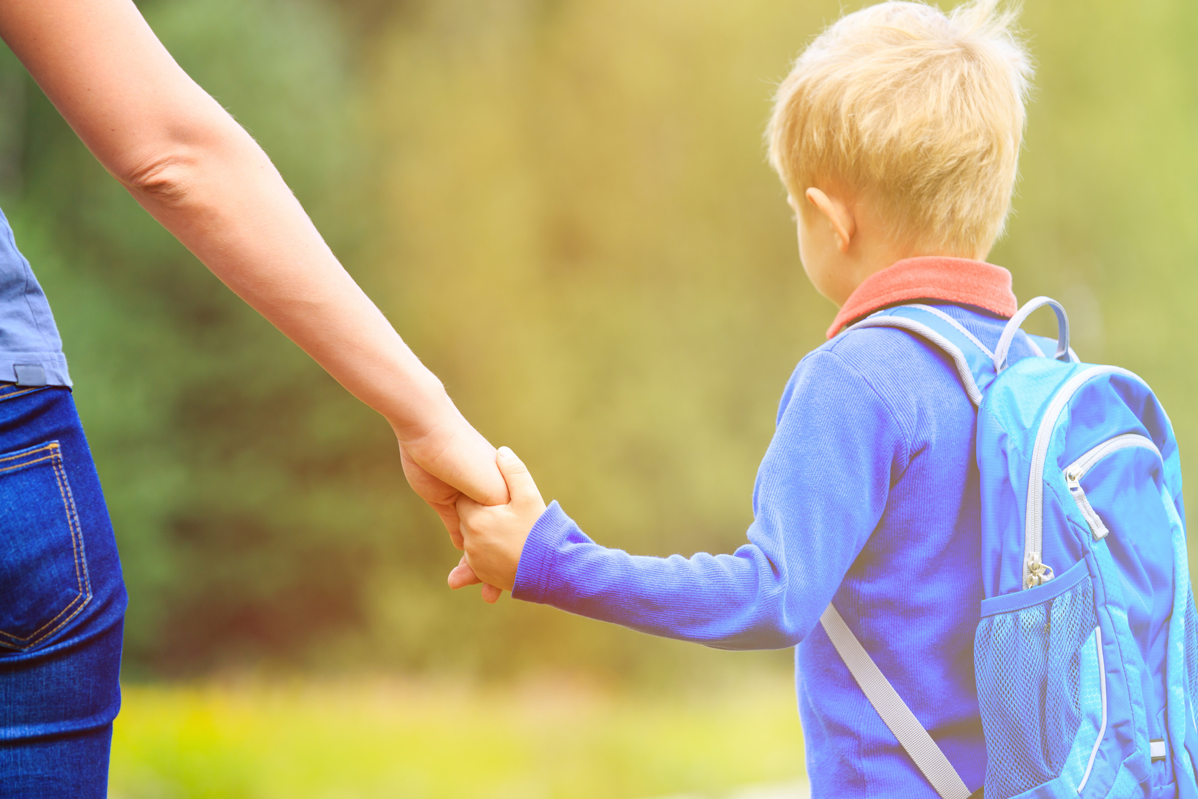 Mother holding hand of little son with backpack outdoors, back to school